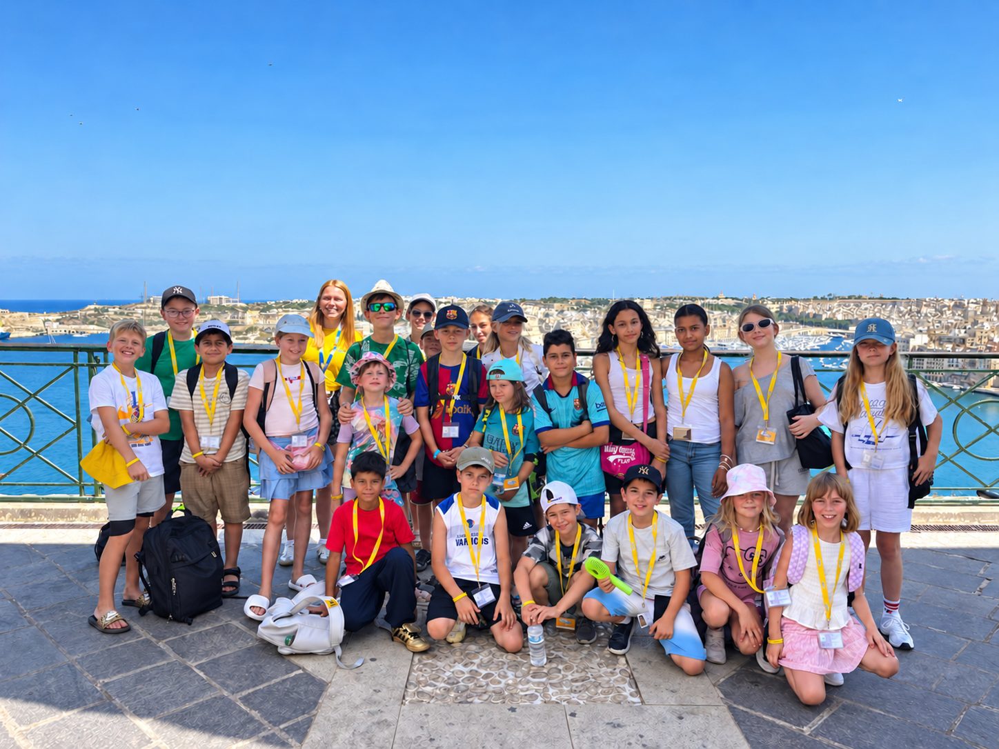 Students wearing yellow lanyards pose for a group photo above Valletta's Grand Harbour during a Malta language course
