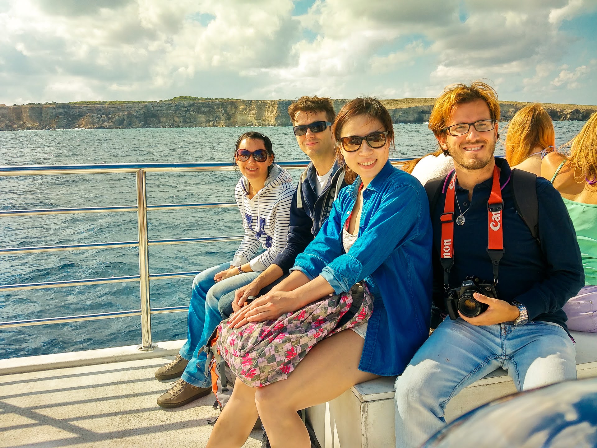 Adult students smiling on a boat excursion along Malta's rugged coastal cliffs