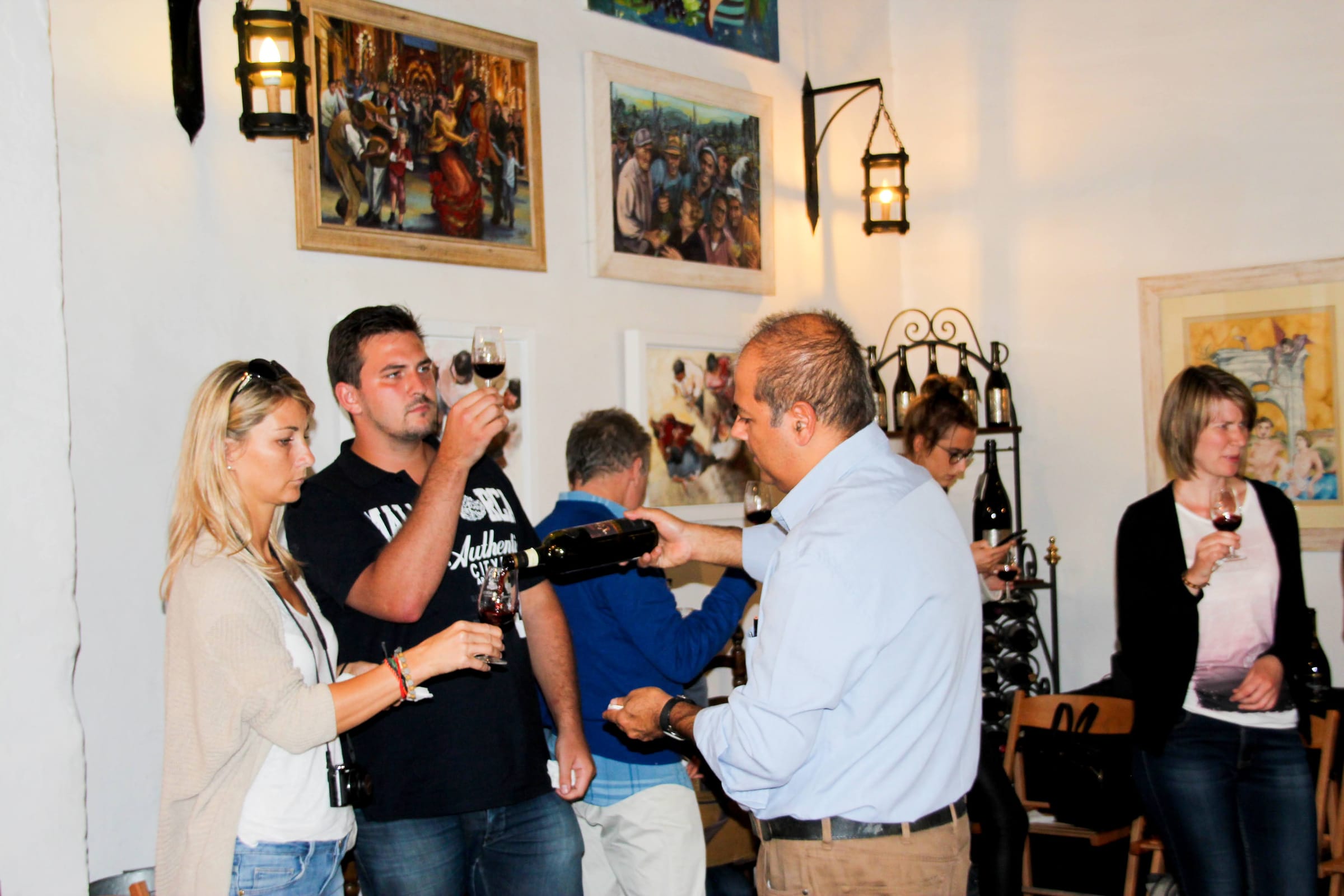 Adult guests enjoying a wine tasting session at a traditional Maltese venue with local artwork on the walls