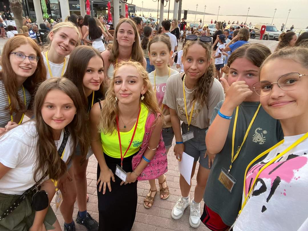 Junior students on lanyards smiling together during an evening walk along Malta's seafront promenade
