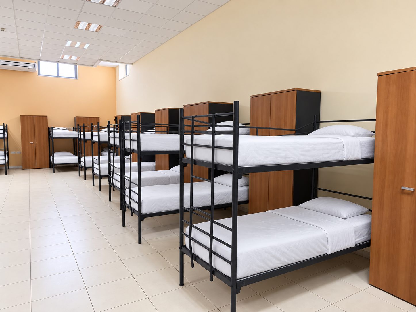 Row of metal bunk beds with wooden wardrobes in a Malta summer camp junior dormitory