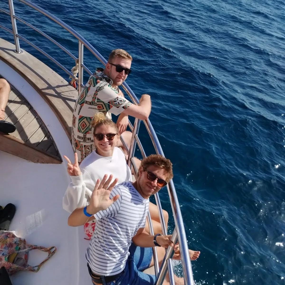 Young adults in sunglasses waving from a boat railing on a Malta sea excursion