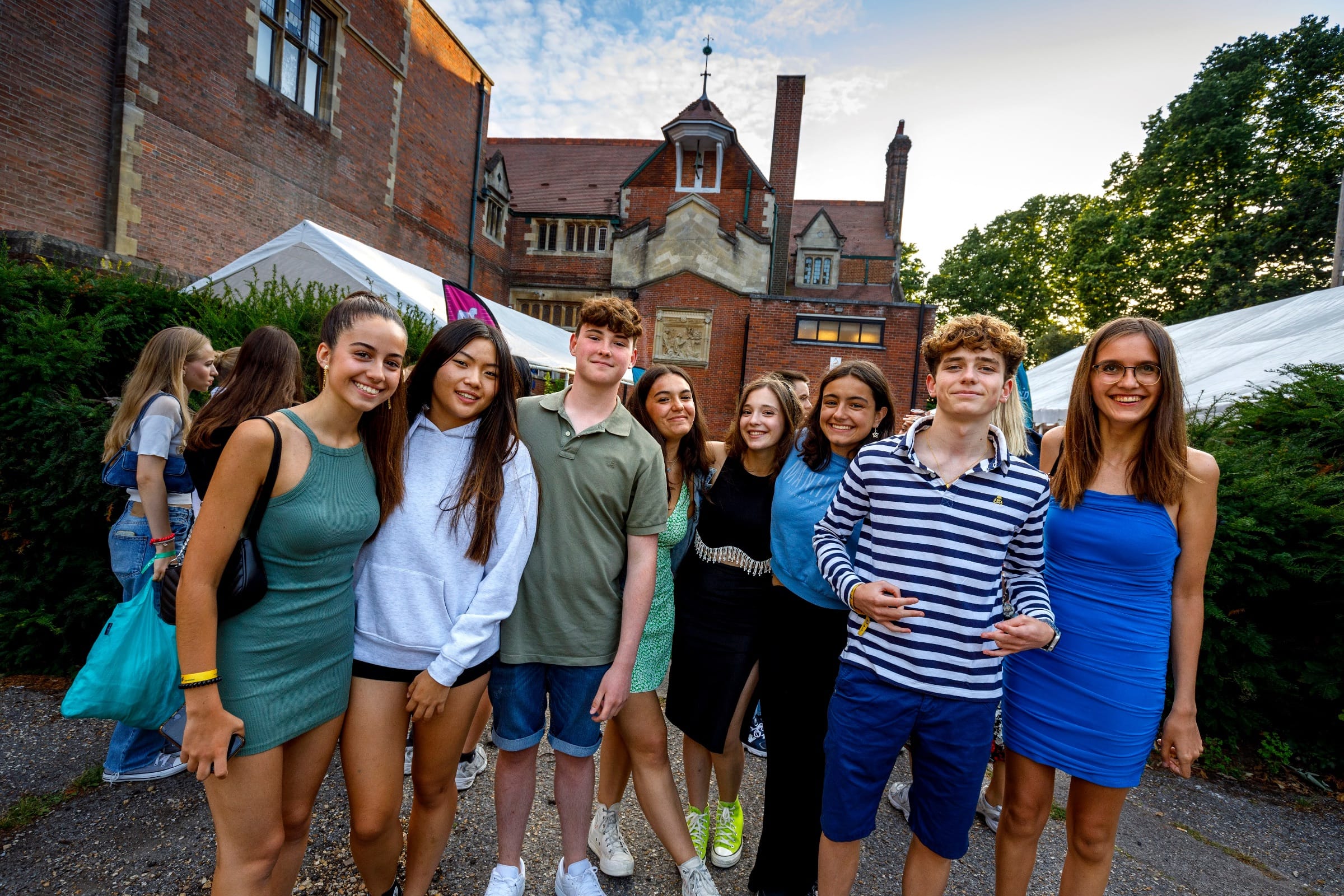 Group of smiling teenage students posing together outside a brick campus building at a Bournemouth summer camp