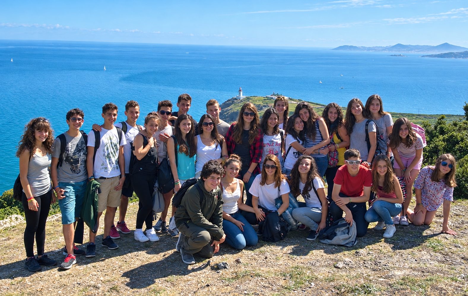 Group of teenage students posing on a coastal clifftop overlooking the Mediterranean Sea during a language trip