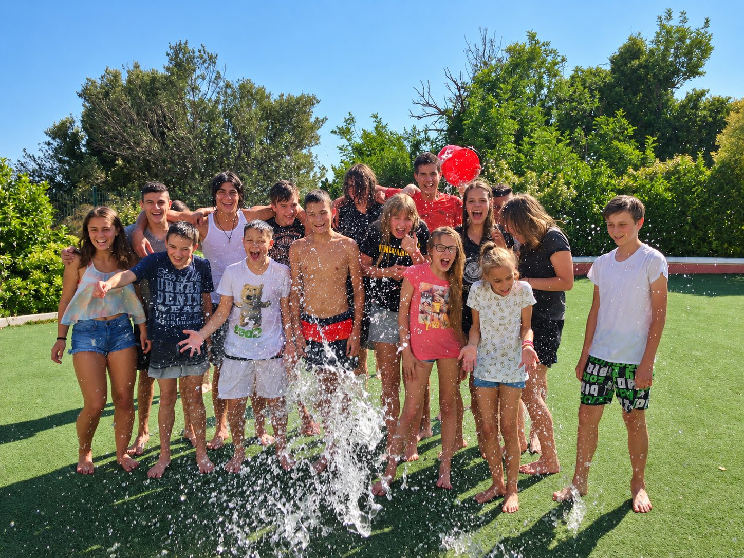 Group of teenage language camp students laughing during a water balloon fight on a sunny lawn