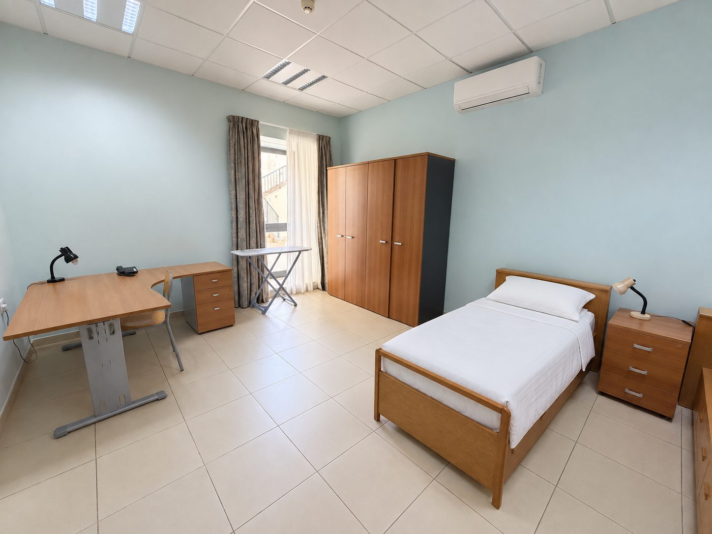 Bright single bedroom with desk, wardrobe and balcony access at a Malta junior summer camp residence