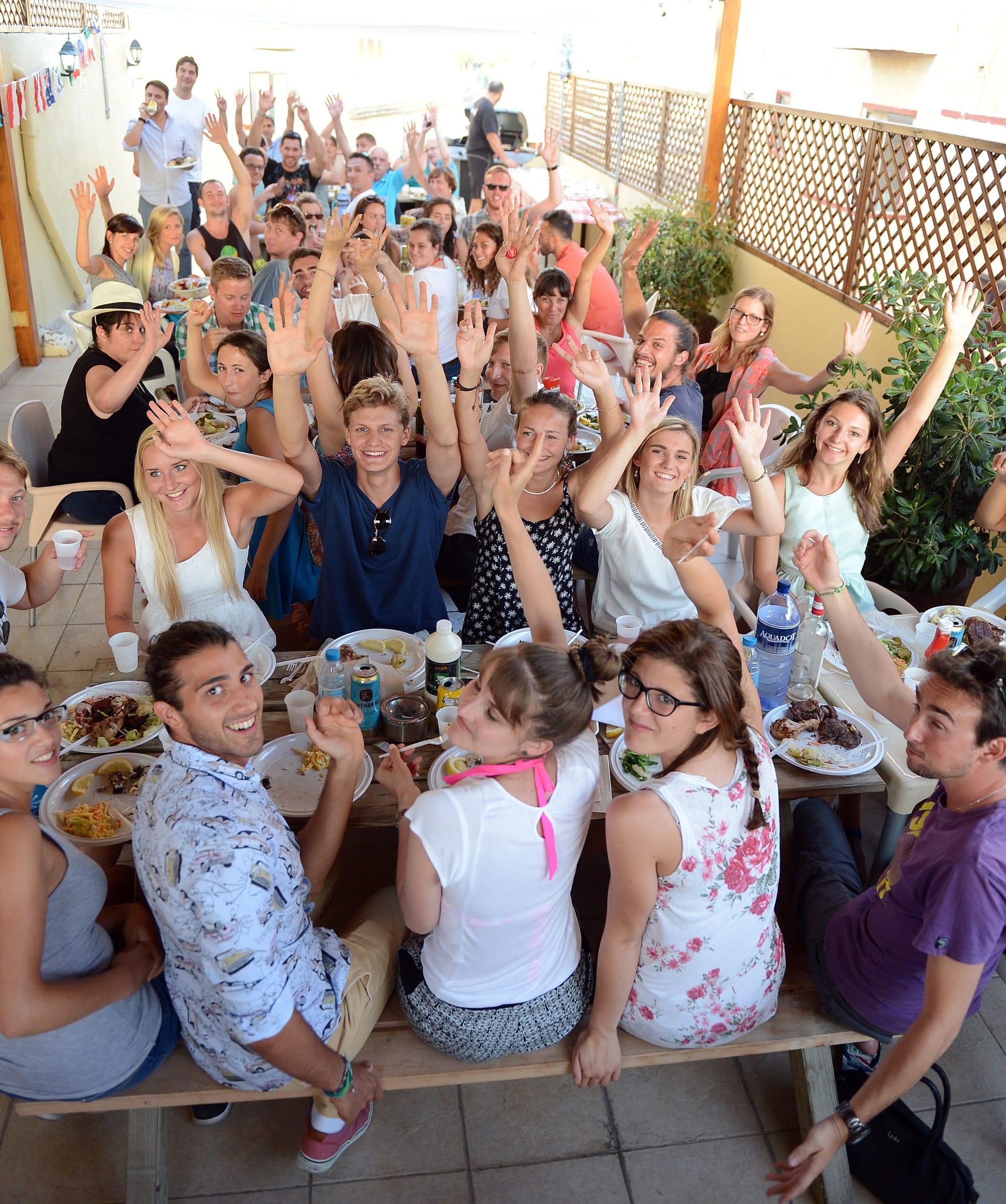 Adult language students cheering with hands raised at an outdoor BBQ party in Malta