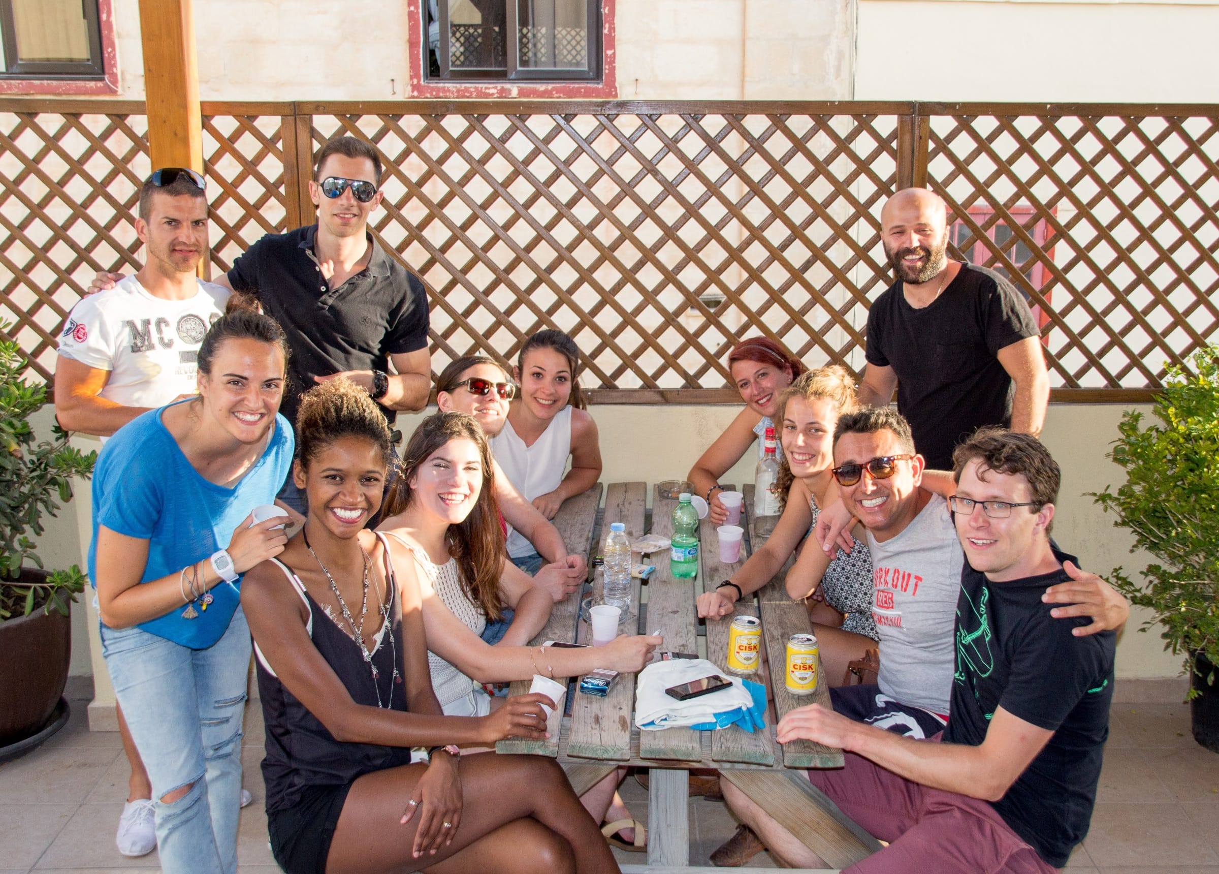 Group of adult language students smiling together at an outdoor table during a social gathering in Malta