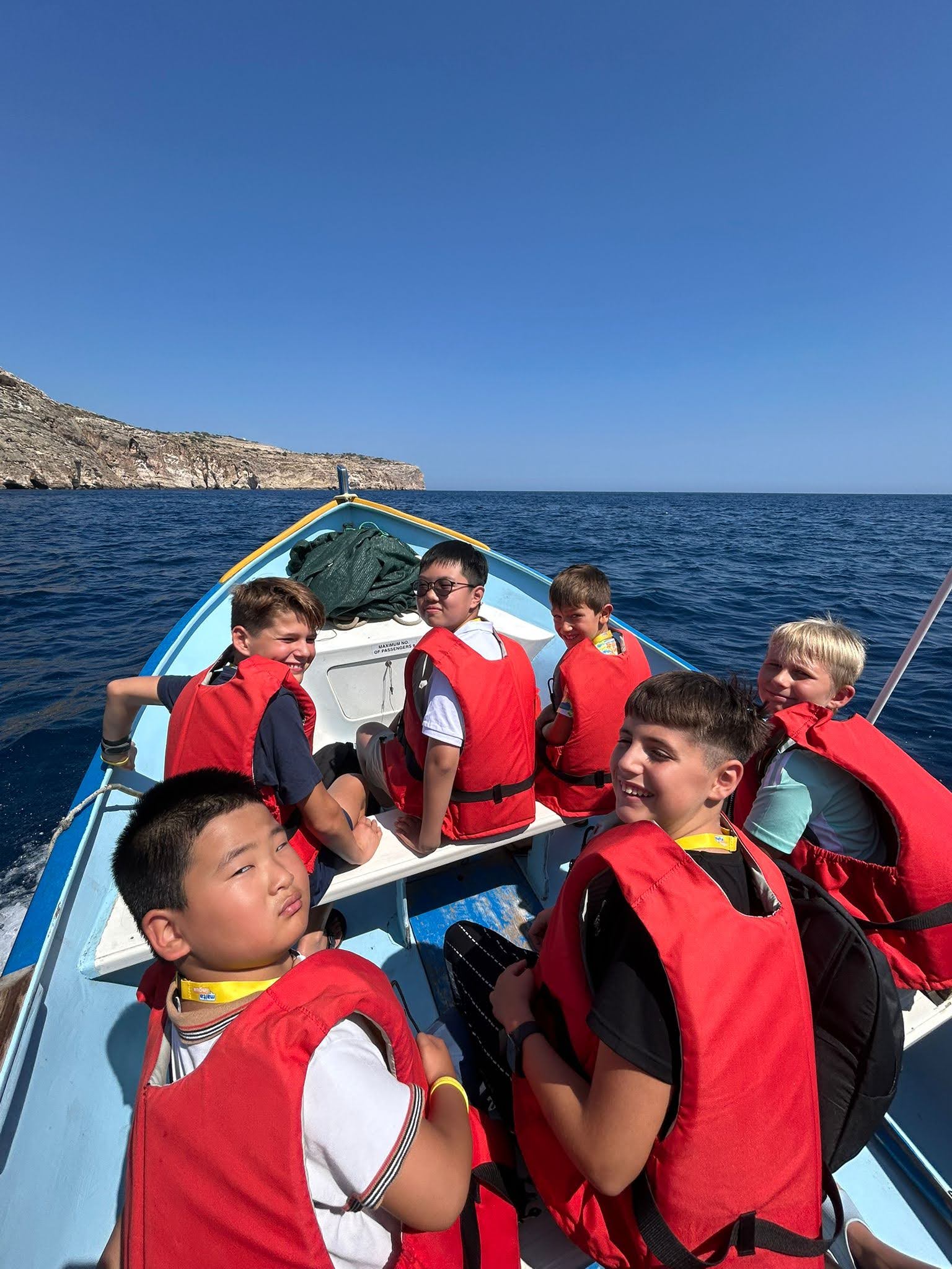 Junior students in red life jackets enjoying a boat excursion along Malta's coastline during their language course