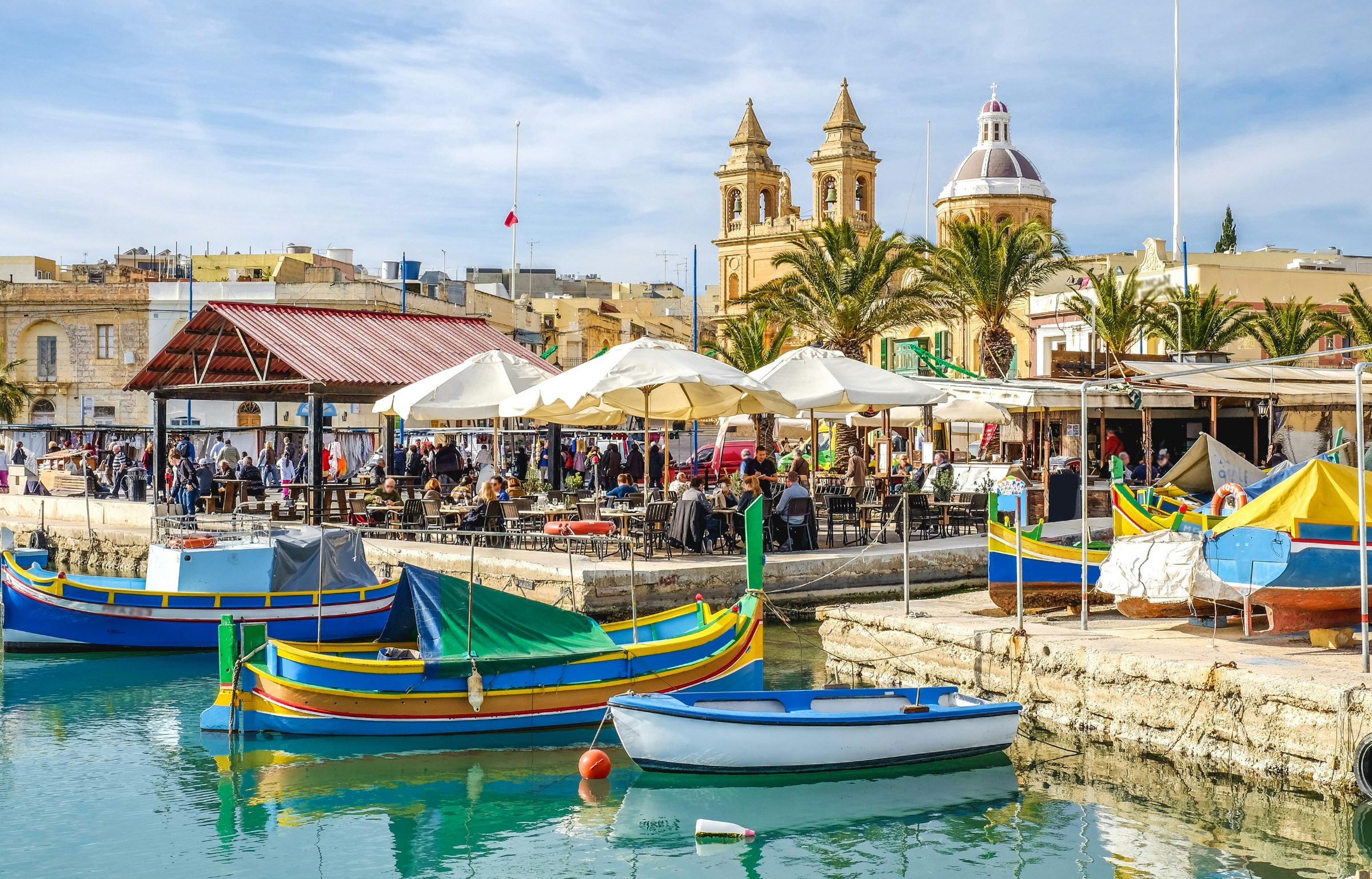 Traditional luzzu fishing boats moored in Marsaxlokk harbour with Malta's church towers in the background
