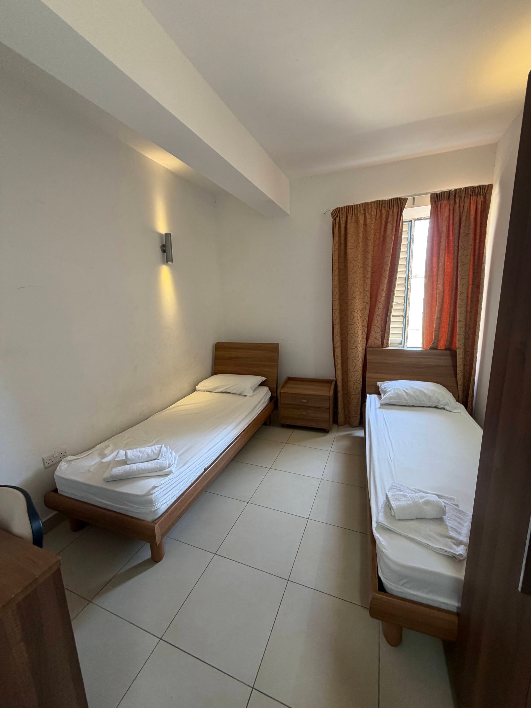 Twin bedroom with two single beds and folded towels at a junior summer camp residence in Malta
