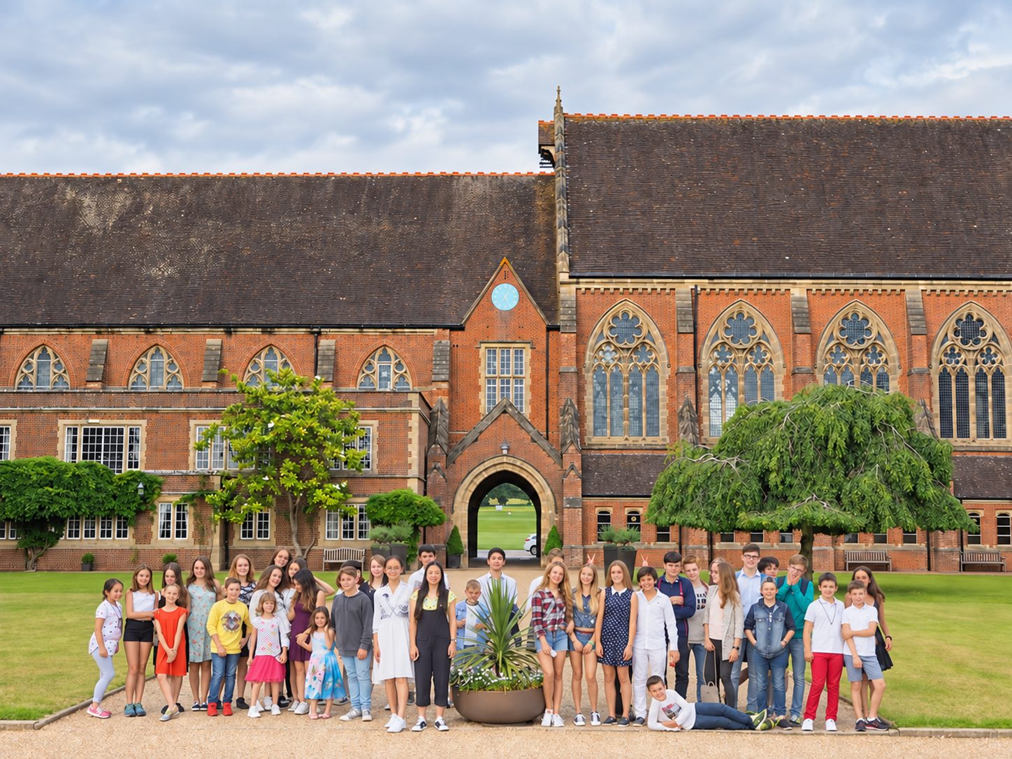 Teenage students posing on a lawn in front of a red-brick Gothic school building during an England language course