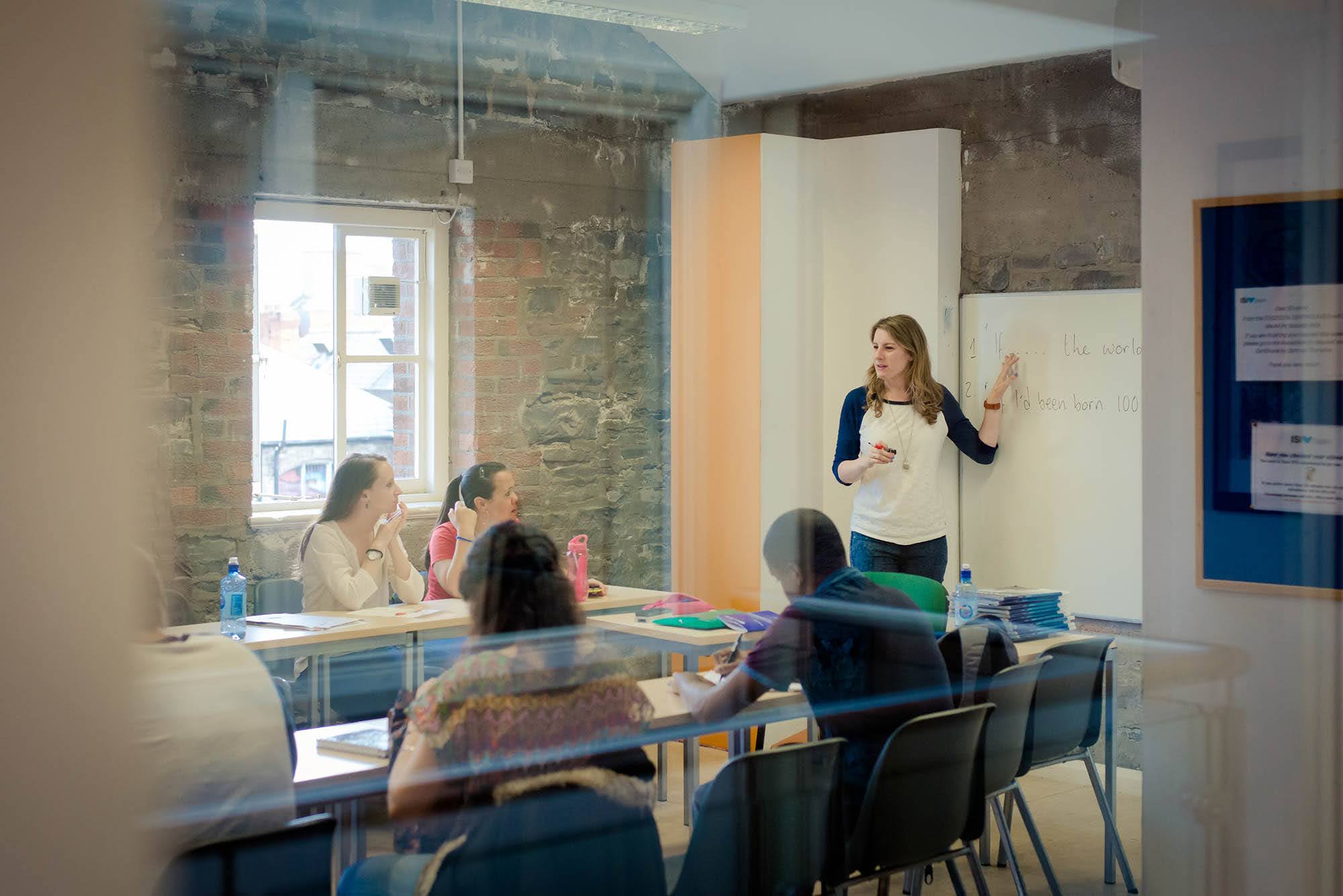 Teacher leading an adult English class, with students seated at desks