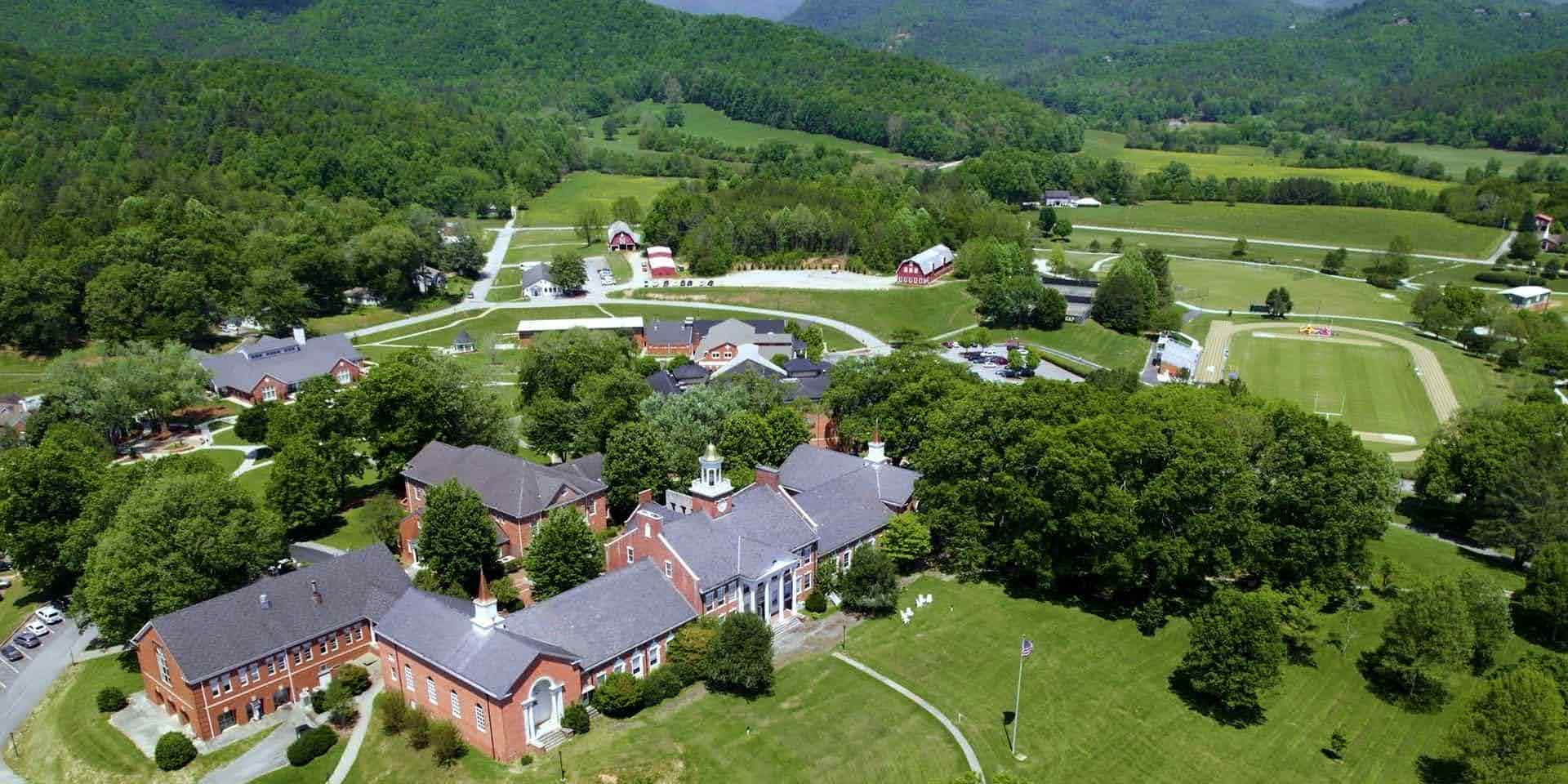 Aerial view of a US boarding school campus surrounded by forested mountains and green fields