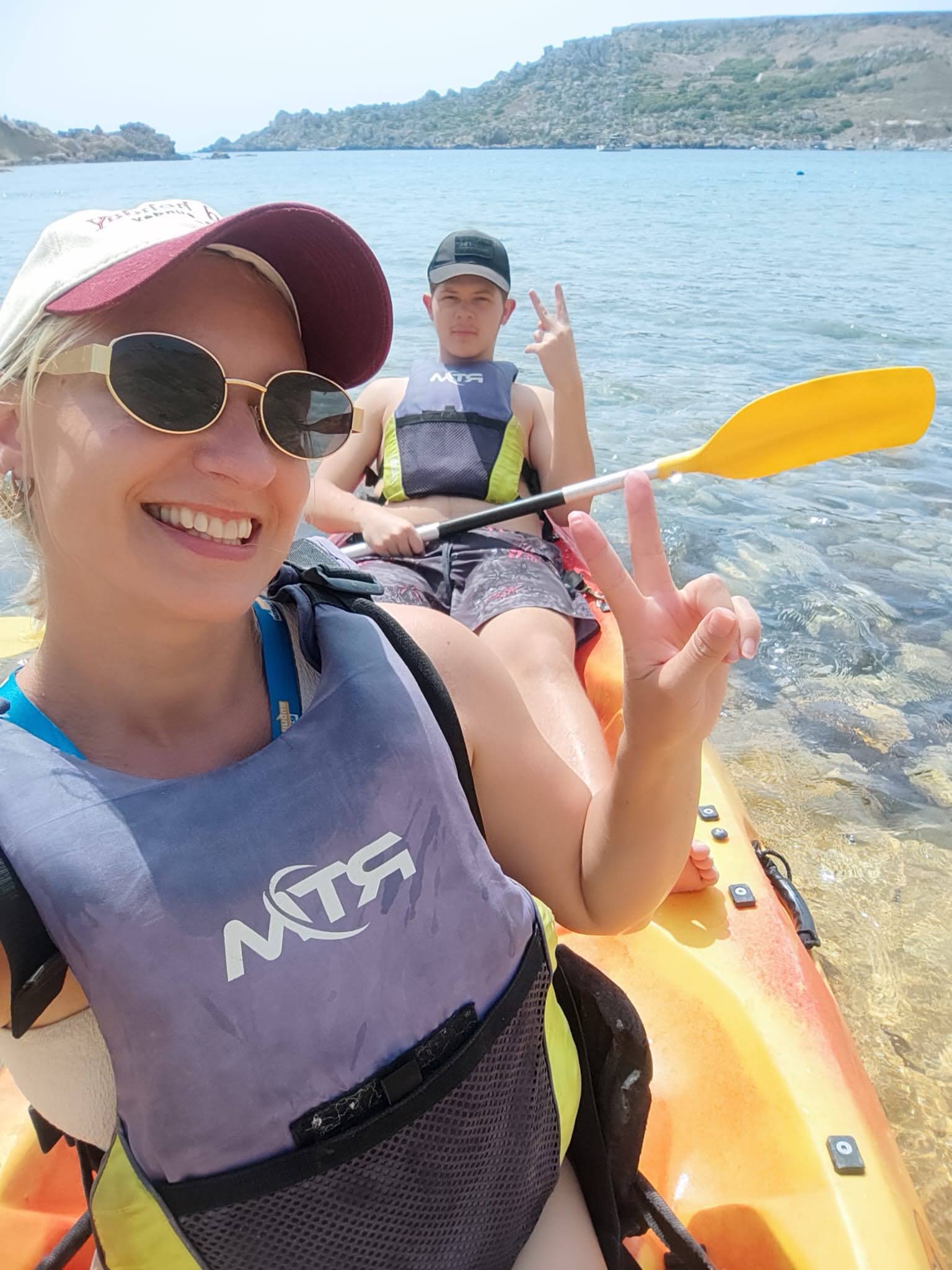 Teen and group leader in life vests giving peace signs while kayaking along Malta's coast