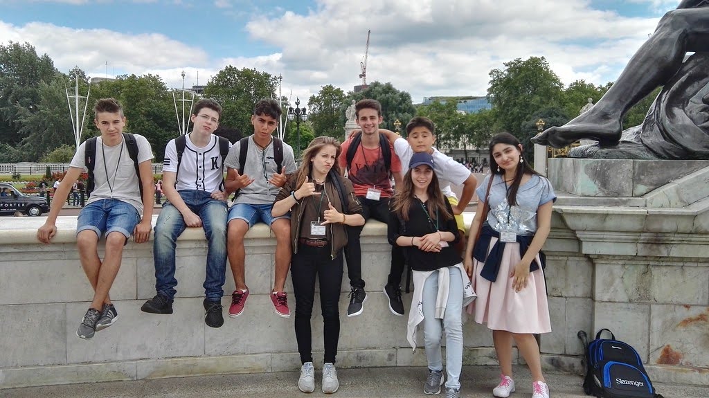 Junior students wearing lanyards pose by a monument during a London city excursion