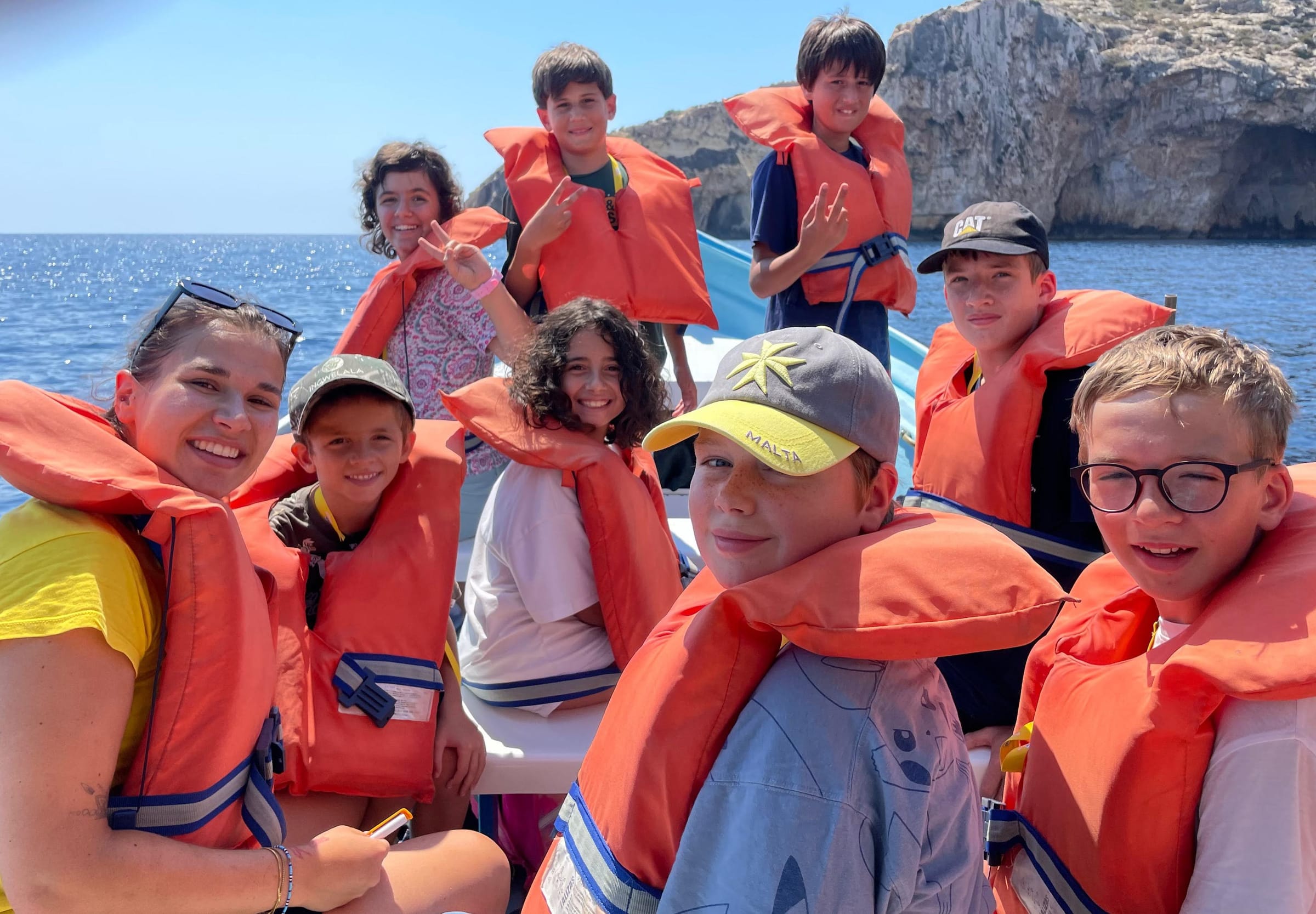 Junior students in life jackets smiling on a boat trip near Malta's rocky coastline