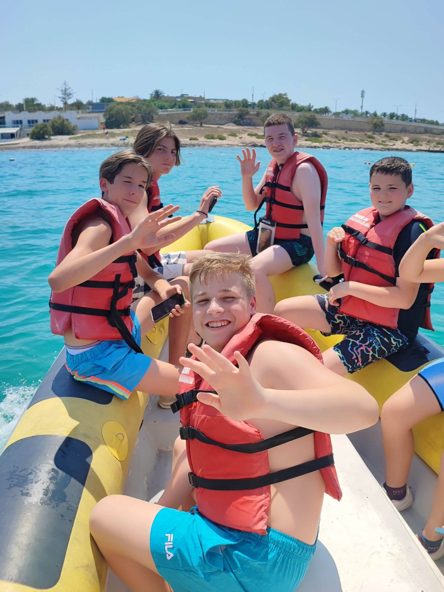 Teen students in life jackets waving from a banana boat during a Malta junior summer course excursion